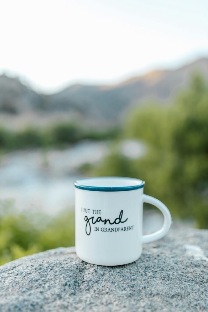 Ceramic mug with 'Grandparent' text sitting on a rock with blurred natural background.