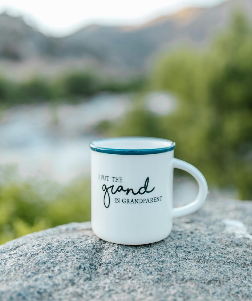 Ceramic mug with 'Grandparent' text sitting on a rock with blurred natural background.