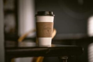 A paper coffee cup with a wooden sleeve on a café table with a blurred background.